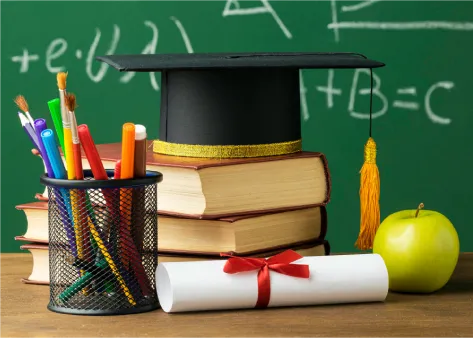Foto contoh: buku, topi wisuda, pensil warna, dan ijazah di depan papan tulis